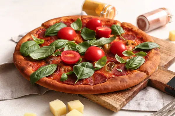 Tahta tahtada domatesli lezzetli biberli pizza ve beyaz arka planda fesleğen.