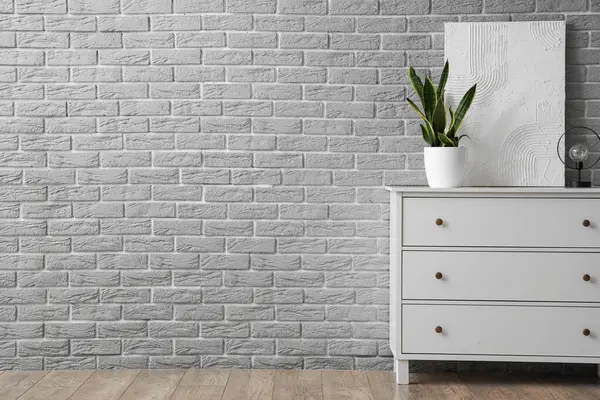 Lambalı dolap, saksı ve gri tuğla duvarın yanındaki tuval.