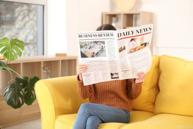 Young woman reading newspaper on sofa at home