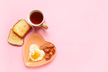Plate with fried egg, tasty bacon, toasts and cup of tea on pink background