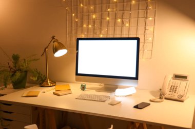 Kırtasiyeli boş bilgisayar monitörü ve gece ofiste parlayan lamba