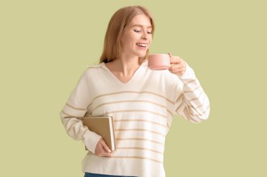 Yeşil arka planda bir fincan çay ve kitapla güzel genç bir kadın.