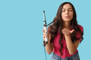 Mavi arka planda saç maşasıyla öpüşen güzel genç bir kadın.