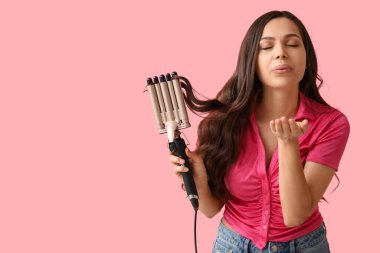 Pembe arka planda saç maşasıyla öpüşen güzel genç bir kadın.