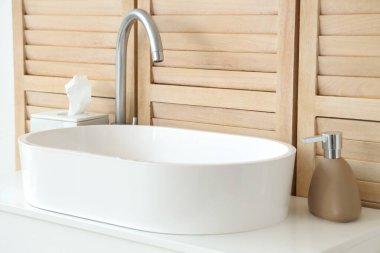 Seramik lavabo ve beyaz çekmeceler banyoda ahşap duvarın yanında.