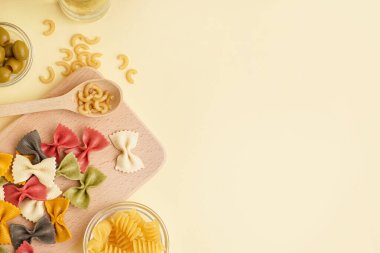 Farklı pişmemiş makarna ve bej arka planda zeytinli kompozisyon