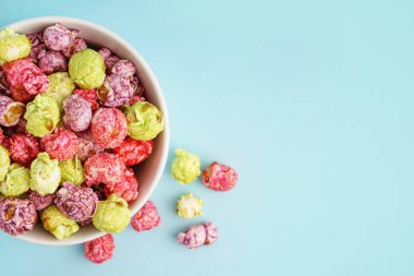 Mavi arka planda tatlı renkli patlamış mısır kasesi