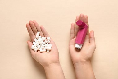 Astım spreyli çocuk elleri ve bej arka planda haplar.