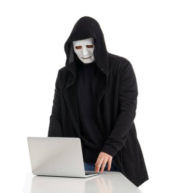 Maskeli hacker beyaz arkaplandaki masada dizüstü bilgisayar kullanıyor