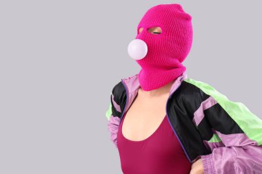 Kar maskeli, gri arka planda sakızı olan güzel, genç ve şık bir kadın.