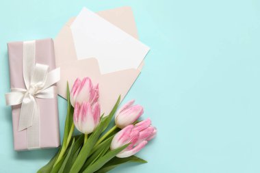 İçinde boş kart, hediye kutusu ve mavi arka planda pembe laleler olan zarf.