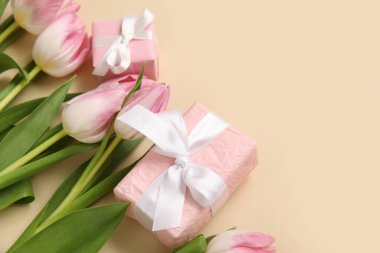 Bej arka planda hediye kutuları olan pembe laleler.