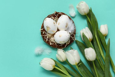 Paskalya yumurtalı yuva, turkuaz arka planda tüyler ve laleler