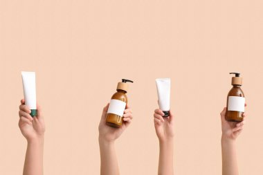 Tüpleri ve şişeleri olan kadın elleri bej arka planda farklı kozmetik ürünler