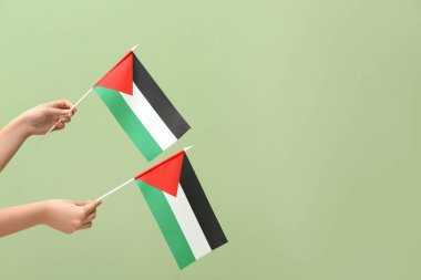 Yeşil arka planda Filistin bayrakları olan kadın eller
