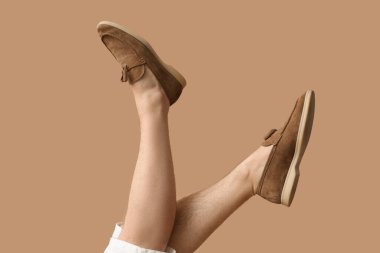 Kahverengi arka planda şık ayakkabılı genç adam bacakları.