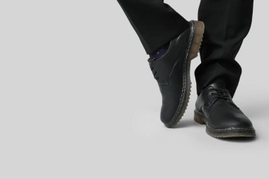 Gri arka planda siyah şık ayakkabılı genç adamın bacakları.