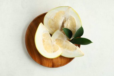 Tahta tabakta taze meyve dilimleri ve beyaz arka planda yapraklar.