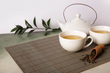 Çaydanlıklı bambu hasırı, bir fincan çay ve beyaz arka plandaki grunge masasında yapraklar.