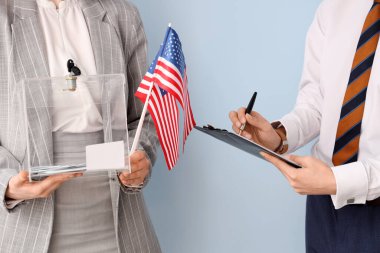 Elinde oy sandığı olan kadın ve ABD bayrakları arka planda panoda yazılı oy pusulası olan adamın yanında. Seçim kavramı