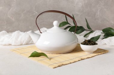 Çaydanlıklı bambu hasırı ve arka planda bir kase kuru çay.