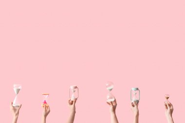 Pembe arka planda kum saati tutan kadın eller.