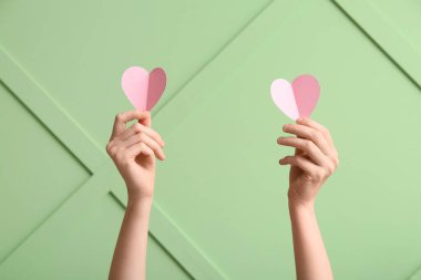 Renk duvarına karşı pembe kağıt kalpli kadın elleri, yakın plan. Sevgililer Günü kutlaması