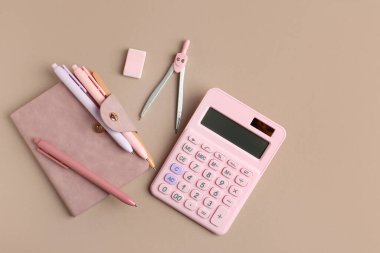 Kalem, pusula, hesap makinesi, not defteri ve silgiyle bej arka planda kompozisyon. Üst görünüm