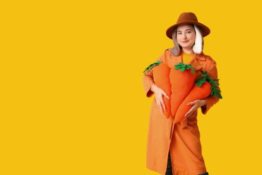 Tavşan kulaklı güzel bir kadın sarı arka planda oyuncak havuç tutuyor. Paskalya kutlaması