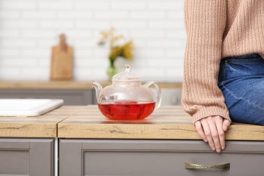 Genç bir kadın mutfaktaki çaydanlığın yanında oturuyor.