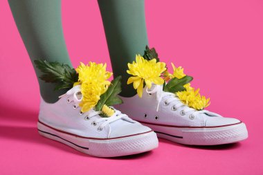 Pembe arka planda sarı kasımpatı çiçekleri olan beyaz ayakkabılı güzel genç kadın bacakları.