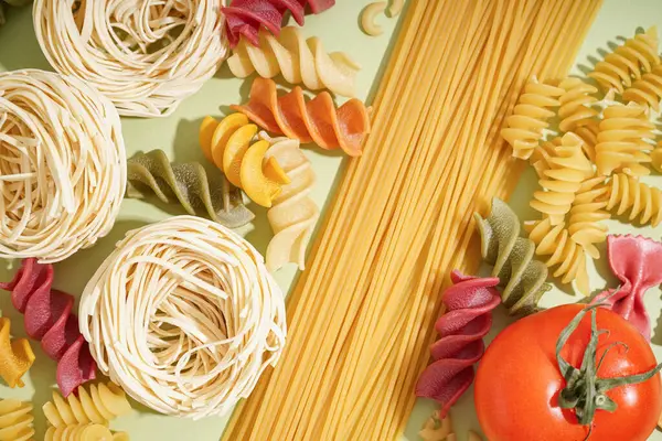 Yeşil arka planda farklı pişmemiş makarna ve domates, yakın plan.