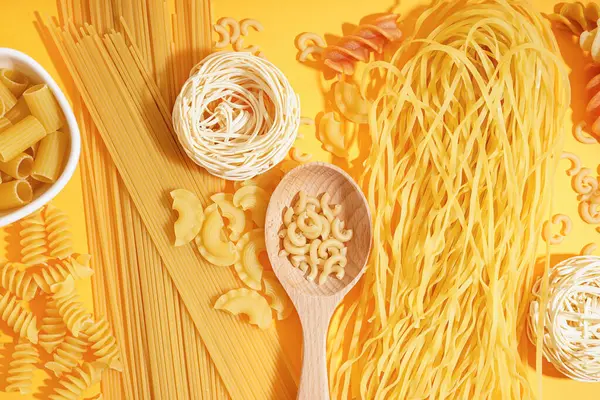 Turuncu arka planda farklı pişmemiş makarna kompozisyonu