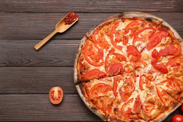 Lezzetli pizza, domates, ahşap kepçe ve ahşap arka planda baharatlar.