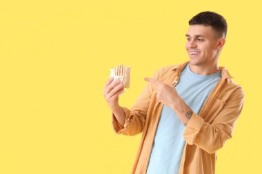 Yakışıklı genç adam sarı arka planda lezzetli bir donör kebabını işaret ediyor.