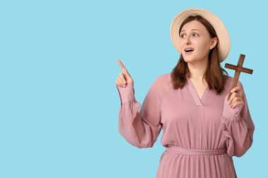 Ahşap haçı olan dindar genç bir kadın mavi arka plandaki bir şeyi işaret ediyor.