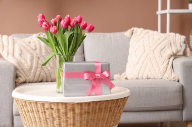 Çiçekli vazo ve hediye paketi oturma odasındaki sehpanın üzerinde.