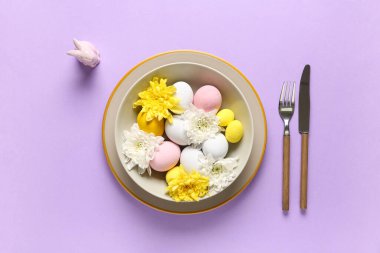 Paskalya yumurtaları ve eflatun arkaplanda kasımpatı çiçekleri olan güzel bir masa.
