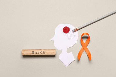 Kağıt insan kafası, kurşun kalem, Kelime Marşı ve gri arka planda turuncu kurdele. Çoklu Skleroz Farkındalık Ayı