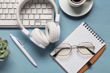 Mavi arkaplanda bilgisayar klavyesi, kulaklık, defter ve gözlük