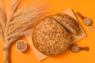 Turuncu arka planda dilimlenmiş somun ekmek, tohum ve buğday dikenli tahta.