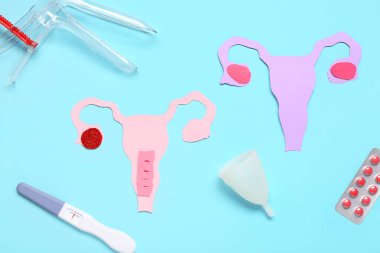 Jinekolojik spekulumlu kağıt uteruslar, mavi arka planda haplar ve hamilelik testi.