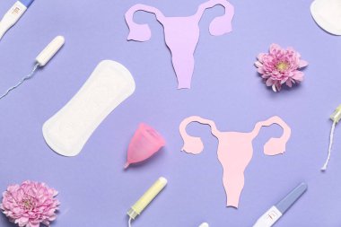 Tamponlu kağıt uteruslar, regl pedi ve mor arka planda fincan.