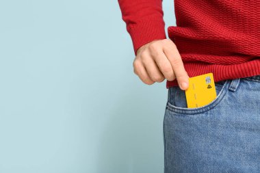 Genç adam kredi kartını mavi arka planda kot pantolonun cebine koyuyor, yakın plan.