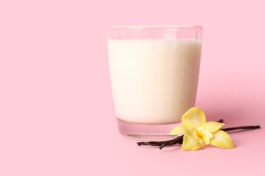 Bir bardak süt, vanilya çubukları ve pembe arka planda çiçek.