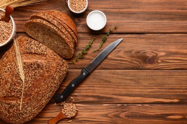 Tahta zemin üzerinde dilimlenmiş somun ekmek, buğday dikenleri, tahıllar ve kekik.