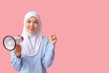 Pembe arka plandaki bir şeyi işaret eden megafonlu genç Asyalı Müslüman kadın. Ulusal Duyulma Günü