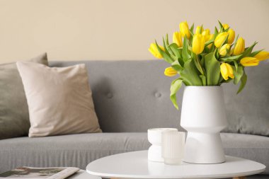 Gri kanepesi ve kahve masasında sarı laleleri olan modern oturma odası.