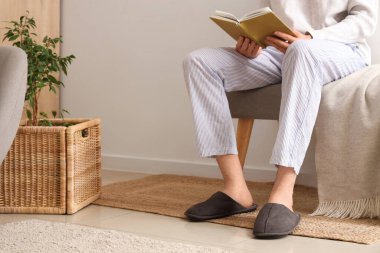 Kitaplı ve terlikli bir adam odada yumuşak bir bankta oturuyor.