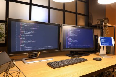 Geceleri karanlık ofiste bilgisayar monitörlü ve tabletli programcı masası.